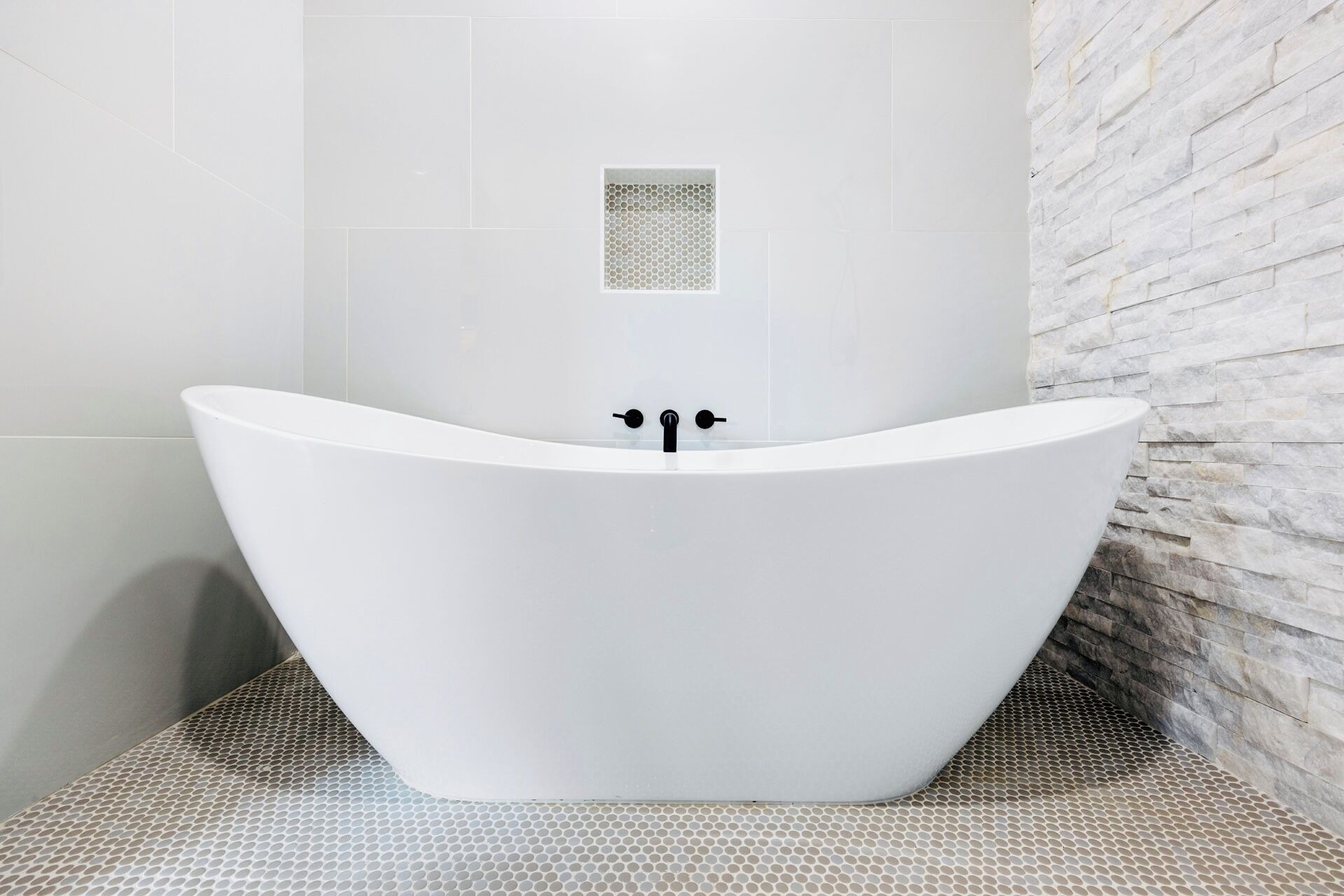 Un baño moderno con una bañera independiente, un ventanal pequeño y una pared de piedra texturizada.