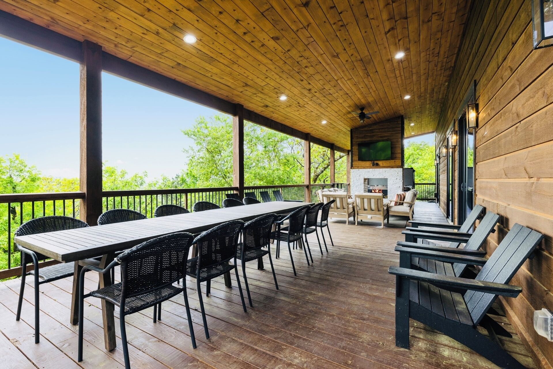 A covered outdoor dining area with a long table and chairs, a grill, and a TV mounted on the wall.