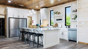 Eine moderne Küche mit weißen Schränken, einem Edelstahlkühlschrank, einer zentralen Kochinsel mit Barhocker und einer Holzbalkendecke.
