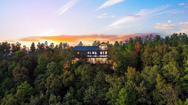 Ein zweigeschossiges Haus, umgeben von dichtem Wald, mit freiem Blick auf den Himmel und Sonnenuntergang.