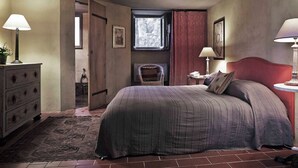 Une chambre à coucher avec un grand lit, deux lampes de chevet, une commode, une chaise et une fenêtre avec des rideaux.