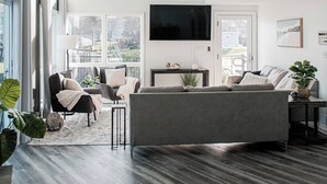 Un salón amplio con un sofá grande de color gris, un televisor de pantalla plana montado en la pared y un ventilador de techo.