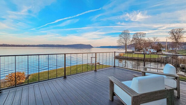Una terraza de madera con vista a un lago y colinas al fondo.