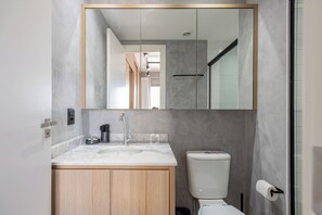 Un baño moderno con un lavabo de mármol, armarios de madera, inodoro y un espejo grande.