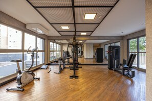 Un gimnasio con máquinas de cardio, equipo de entrenamiento de pesas y amplios ventanales que proporcionan luz natural.
