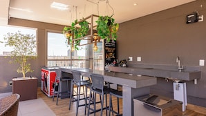 A modern kitchen with a bar area, bar stools, a large window, and a potted plant. - NOV - NEXT ONE Vila Nova Conceição (São Paulo)