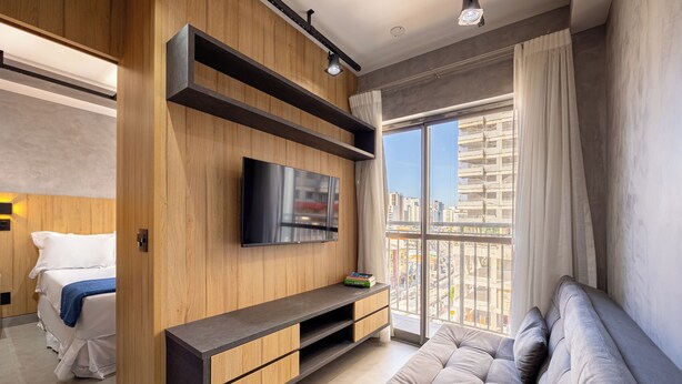 A modern living room with a large window, a flat-screen TV, and a built-in entertainment unit. - NOV - NEXT ONE Vila Nova Conceição (São Paulo)