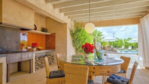 A round glass table with wicker chairs, a hanging light fixture, and a view of a pool and greenery. - Country House 'Son Puca 1' with Private Pool, Wi-Fi and Air Conditioning (Illes Balears)