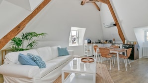Ein Loft-Wohnraum mit weißem Sofa, Esstisch, Stühlen, einer Küchenzeile und einem großen Fenster.