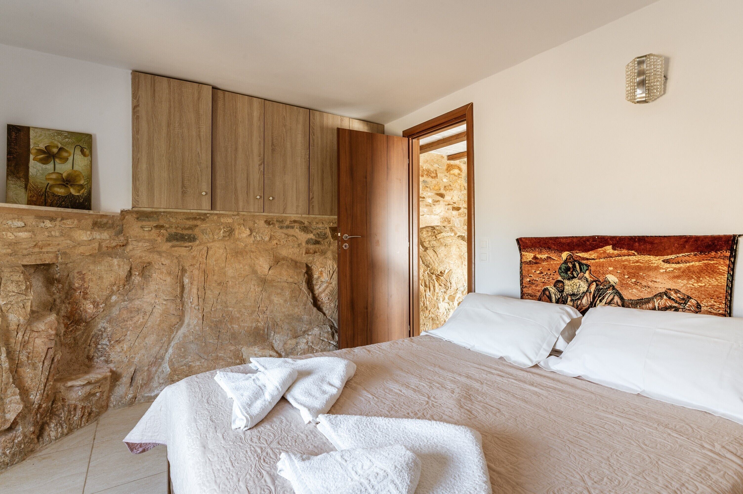 A bedroom with a stone wall, wooden wardrobe, and a bed with white linens.