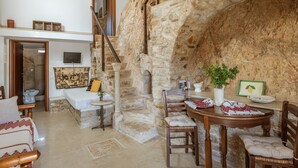 Una habitación rústica con pared de piedra, escalera de madera, una cama, una mesa de comedor con sillas y una mesita con una planta.