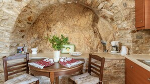 Una habitación con paredes de piedra, una mesa redonda, sillas, una cafetera y un armario.