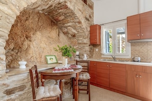 Eine Küche mit Steinsandsteinwänden, Holzschränken, einem Esstisch mit Stühlen und einem Fenster mit Fensterläden.