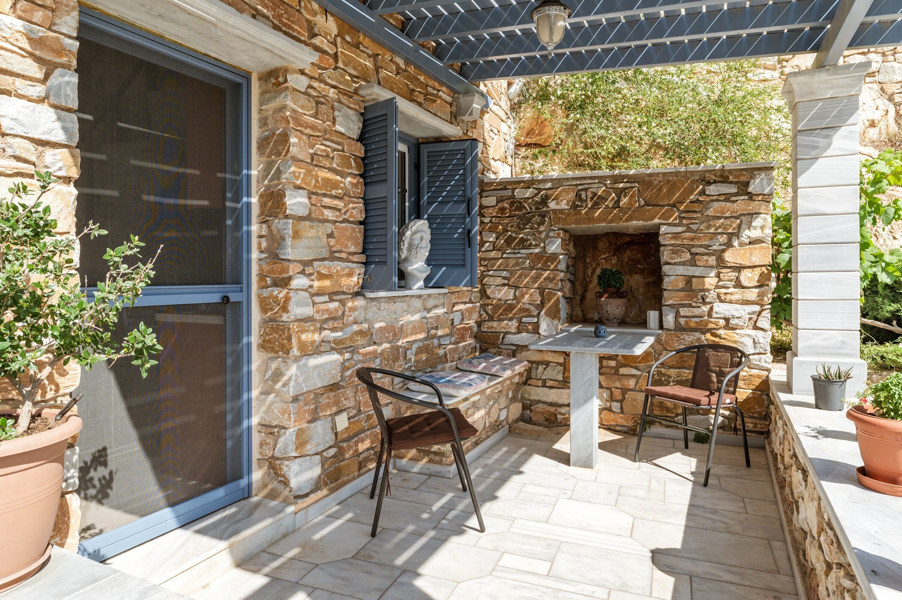 A stone patio with a table and chairs, a stone fireplace, and a pergola with solar panels.