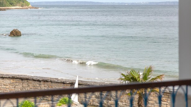 A coastal view with a stone wall, a rock in the water, and a distant shoreline. - Apartment 'Sea View on the Beach' with Sea View, Shared Pool and Wi-Fi (Douarnenez)