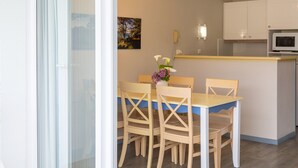 A dining area with a table and chairs, a kitchen with cabinets and a microwave, and a painting on the wall. - Apartment 'Sea View on the Beach' with Sea View, Shared Pool and Wi-Fi (Douarnenez)