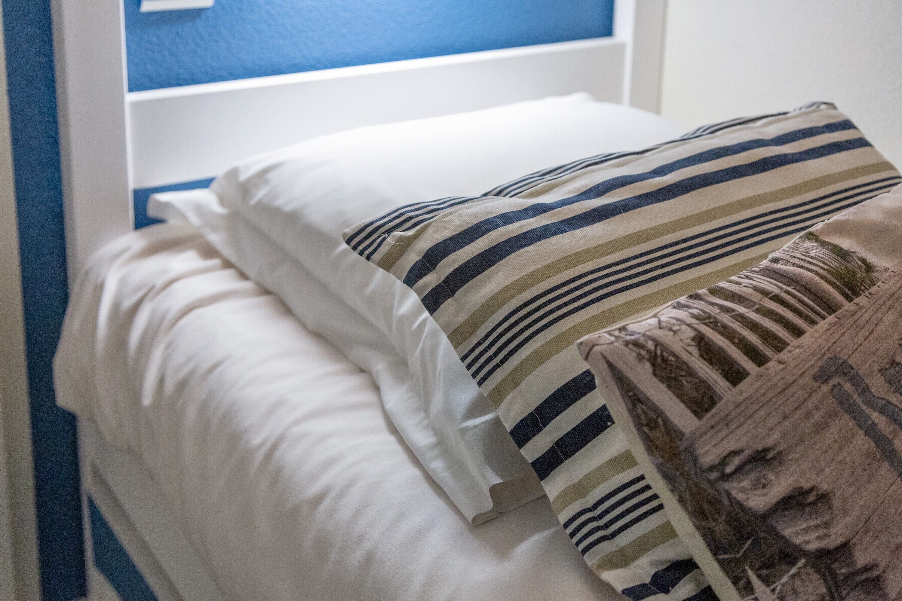 A bed with white bedding and striped pillows.