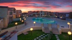 A pool surrounded by buildings with steps leading to the pool, and a sunset in the background.