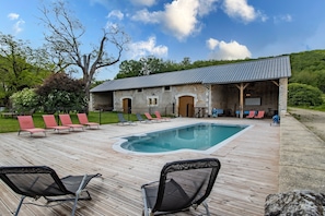 A pool area with lounge chairs, a building with a metal roof, and a wooden deck. - Cottage 'Gîte 3' with Mountain View, Shared Pool and Wi-Fi (Condat-sur-Vézère)