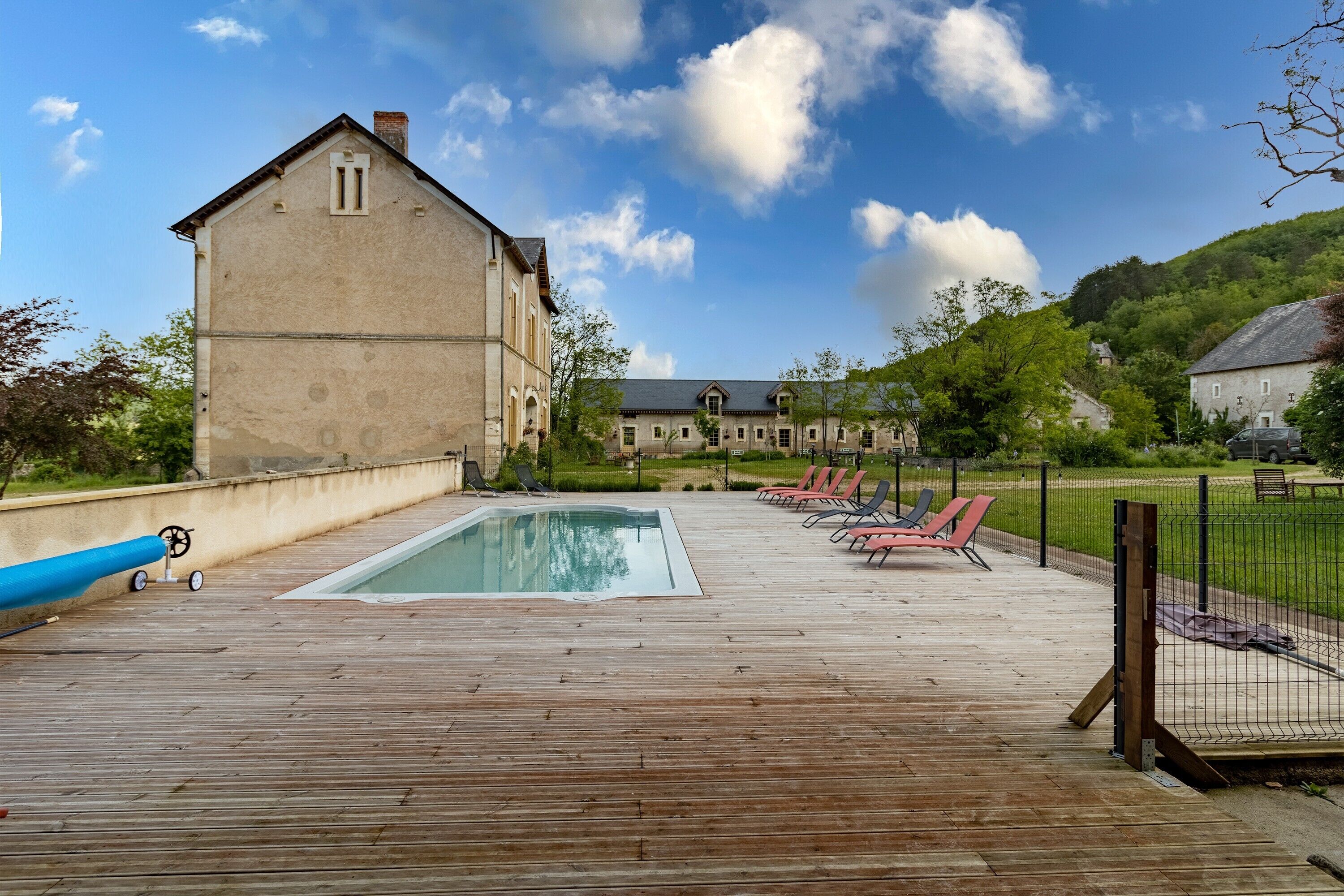 A wooden deck with a swimming pool, lounge chairs, and a large building in the background.