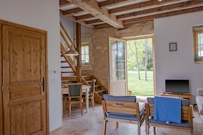 A room with a stone wall, wooden ceiling beams, a TV, and a dining area with chairs and a table. - Cottage 'Gîte 3' with Mountain View, Shared Pool and Wi-Fi (Condat-sur-Vézère)