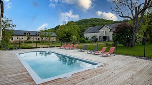 A swimming pool with lounge chairs, a wooden deck, and a large building in the background.