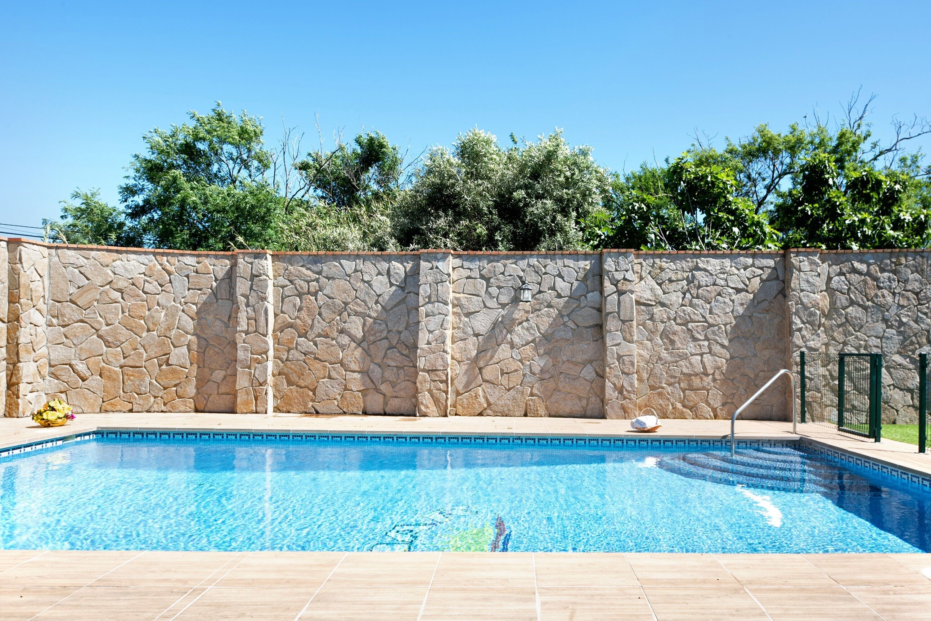 Una piscina con muros de piedra y solárium empedrado.