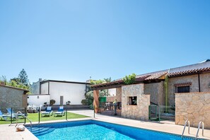 Una piscina con sillones de descanso, un edificio de piedra y un cielo azul despejado.