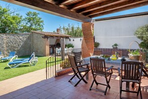 An outdoor patio with a table and chairs, a barbecue grill, and a stone wall.