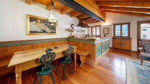 A wooden dining table with chairs, a kitchen area with a stove, and a window with a view. - Apartment 'Casa San Giovanni 2 A Vinigo' with Mountain View, Balcony and Wi-Fi (Vinigo)