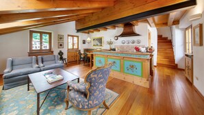 A spacious loft with a high ceiling, wooden beams, a kitchen with green cabinets, a dining area with a sofa and chairs, and a staircase leading to an upper level. - Apartment 'Casa San Giovanni 2 A Vinigo' with Mountain View, Balcony and Wi-Fi (Vinigo)