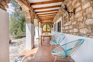 A covered patio with stone walls, wooden beams, a table, and two chairs. - Holiday Home 'Can Favo' with Mountain View, Private Pool and Air Conditioning (Copons)