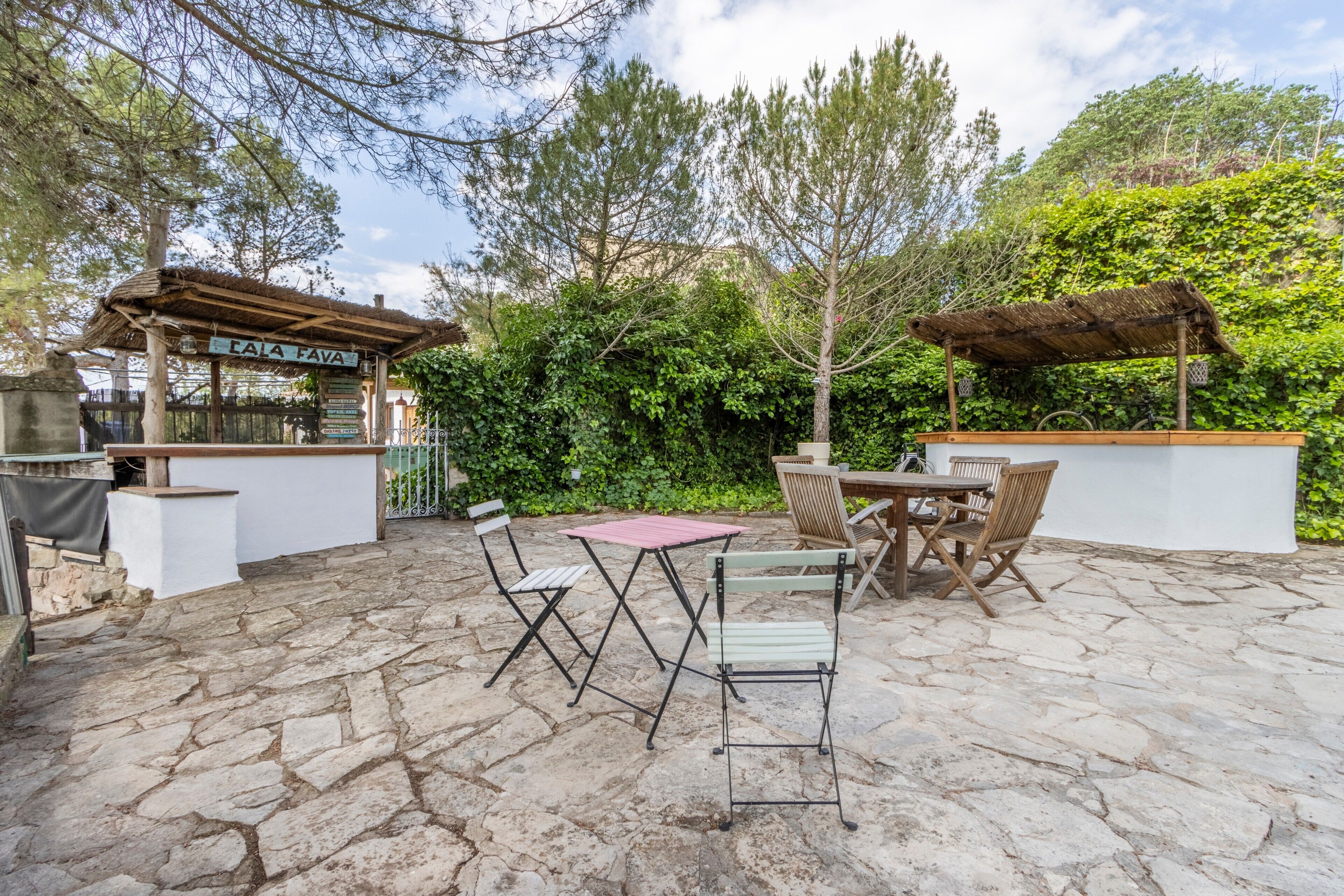 Un patio exterior con suelo de piedra, un pérgola y una mesa de madera con sillas.