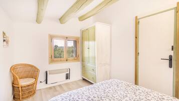 Un dormitorio con cama, una silla de mimbre, un armario, un radiador y una ventana.
