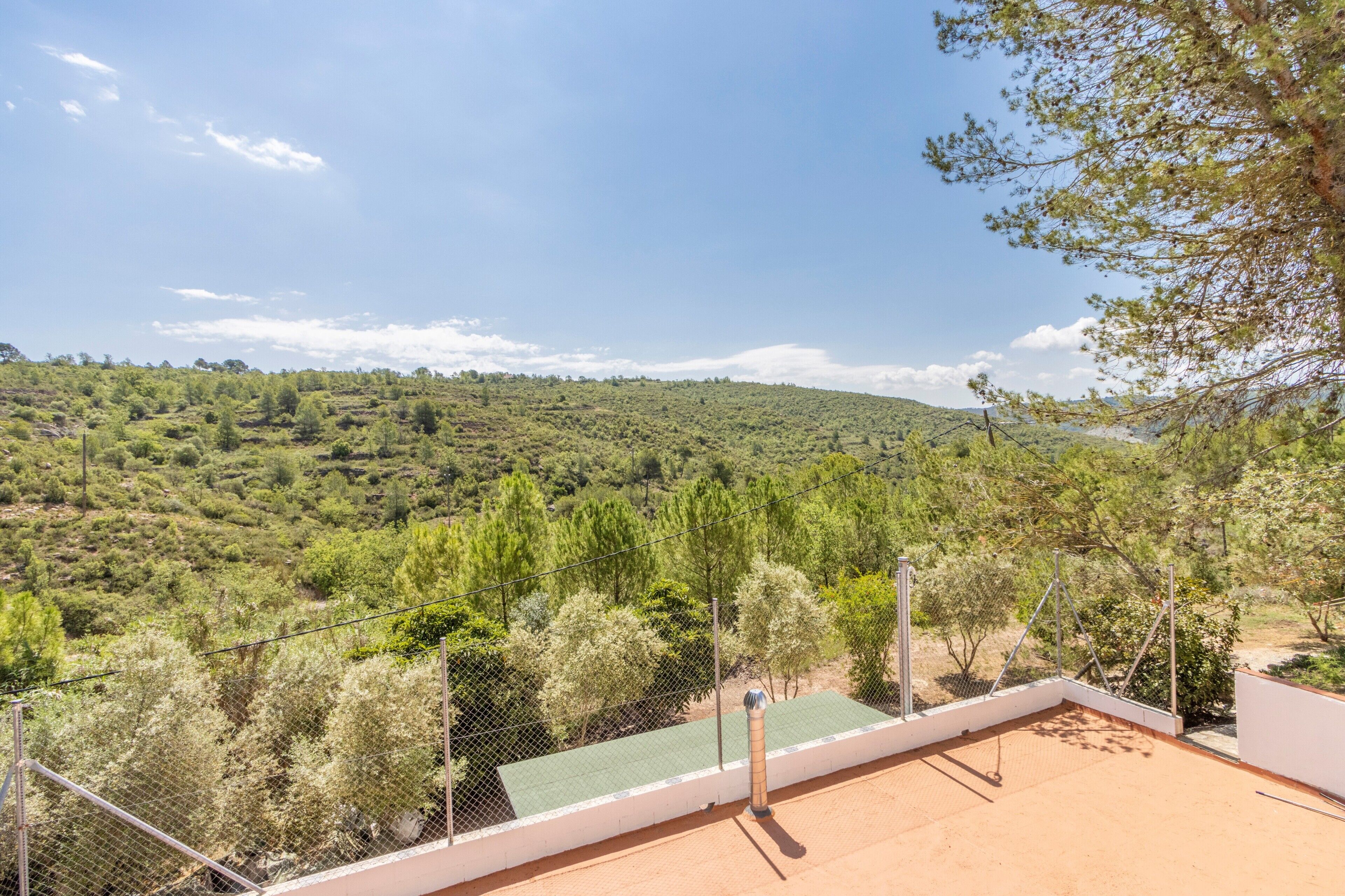 A terrace with a view of a hilly landscape, a metal fence, and a green roof.