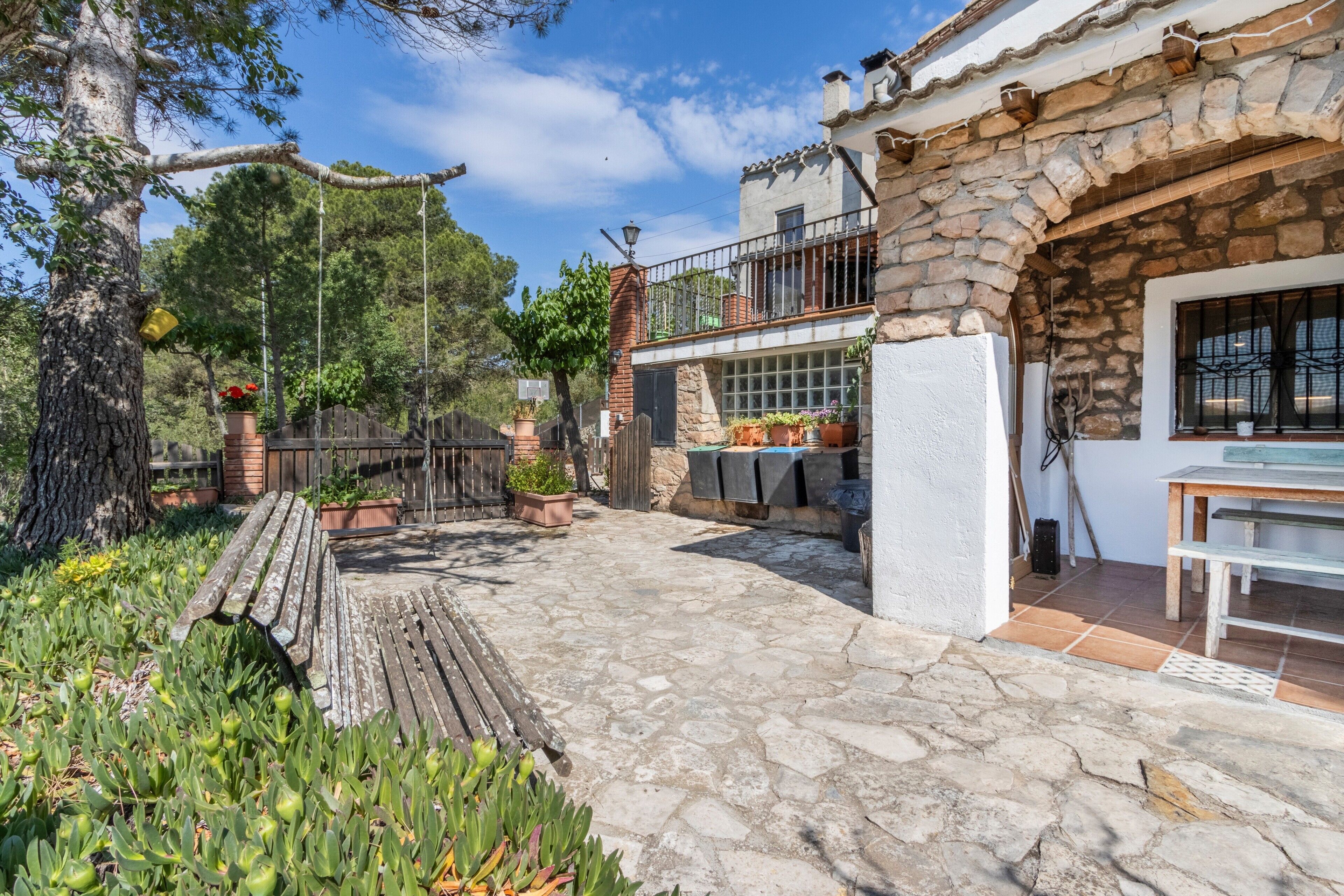 Une terrasse en pierre avec un banc en bois, des plantes en pot et un balcon doté d’une balustrade.
