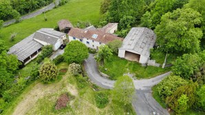 Vista aérea de uma propriedade rural com vários edifícios, uma estrada sinuosa e vegetação ao redor.