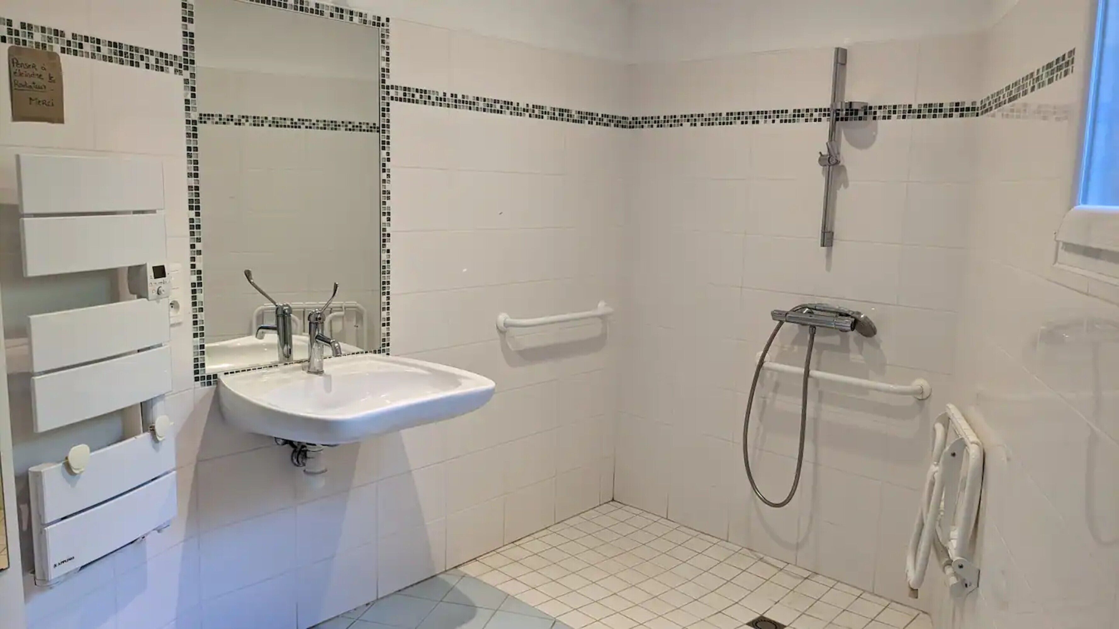 A bathroom with a white sink, a mirror, a shower, and a towel rack.