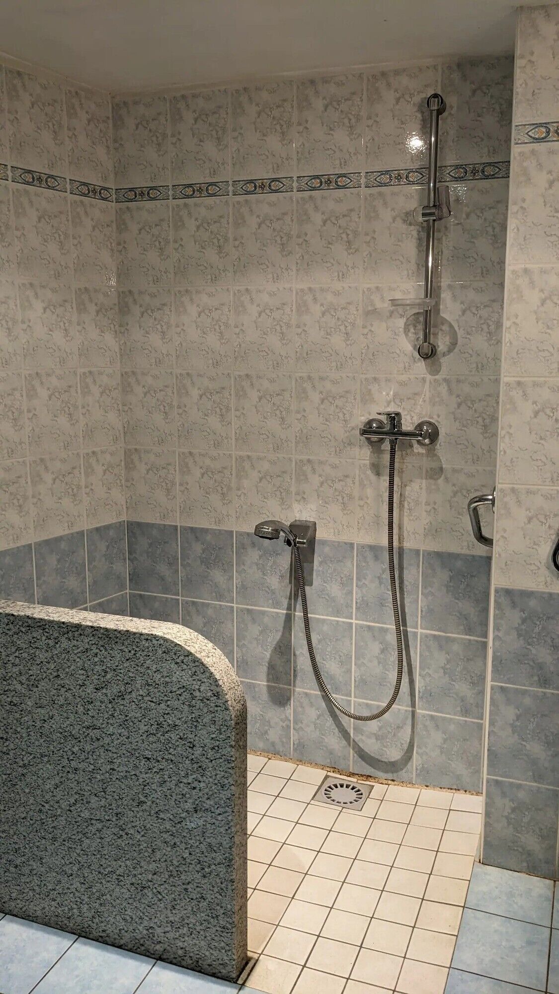 Un espace douche comprenant une baignoire en granit, un pommeau de douche à main et un pommeau de douche fixé au mur.