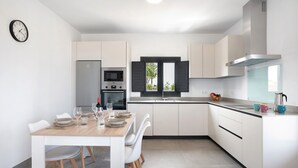 A modern kitchen with white cabinetry, a dining table set with plates and glasses, and a microwave. - Holiday Home 'Casa Valle' with Private Pool, Wi-Fi and Air Conditioning (Conil de la Frontera)