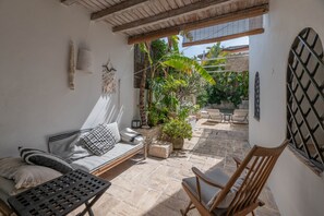 Un patio con un sofá, una silla de madera y plantas en macetas.