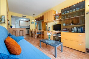 A living room with a sofa, coffee table, TV, kitchen area, and wooden cabinets.