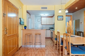 A kitchen with wooden cabinets, a central island with stools, a dining area with a table and chairs, and a clock on the wall.
