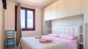 A bedroom with a bed, a chair, a window, and built-in storage. - Holiday Home 'Calypso Sea View Holiday House 2' with Sea View, Wi-Fi and Air Conditioning (Badesi)