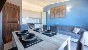 A modern kitchen with white cabinets, a dining table set with black bowls and plates, and a blue wall with a world map. - Holiday Home 'Calypso Sea View Holiday House 2' with Sea View, Wi-Fi and Air Conditioning (Badesi)