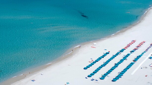 An aerial view of a beach with rows of blue umbrellas and white sand. - Holiday Home 'Calypso Sea View Holiday House 2' with Sea View, Wi-Fi and Air Conditioning (Badesi)