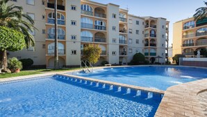 Una piscina con borde de azulejos, rodeada por un edificio de varios pisos con balcones y una palmera.