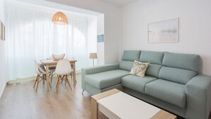 Una sala de estar con un sofá, una mesa de comedor con sillas, una lámpara colgante y un cuadro en la pared.