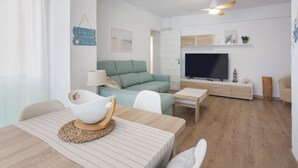 Una sala moderna con sofá, televisión, mesa de comedor y ventilador de techo.