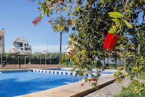Una piscina con borde de piedra, rodeada de vegetación y un cielo azul despejado.